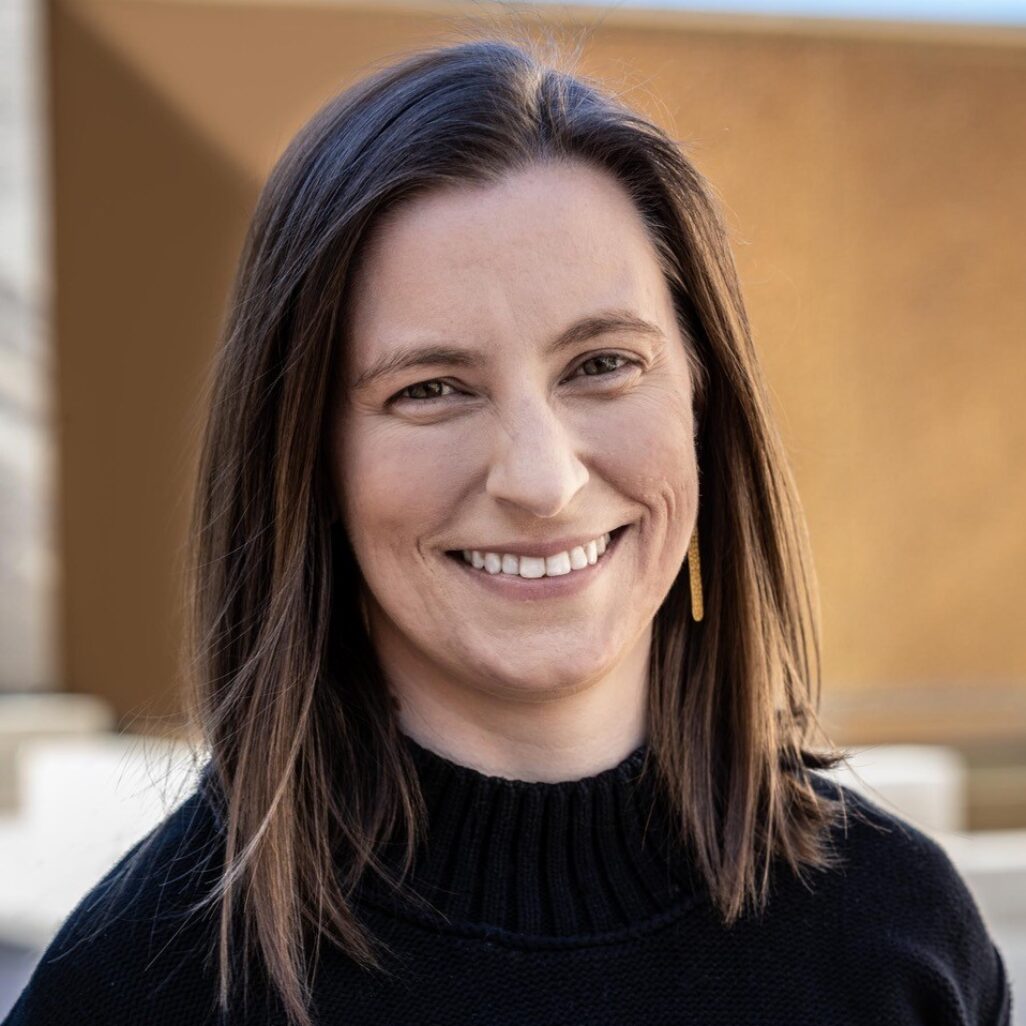 Clare Kobasa, with shoulder-length brown hair, wears a black turtleneck and smiles for a headshot.