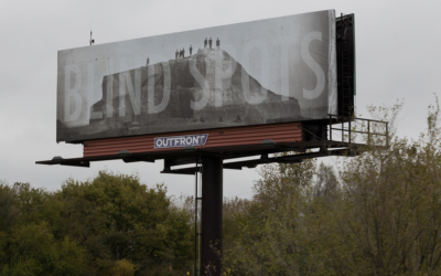 Billboard of people standing on a large mound with words "Blind Spots"