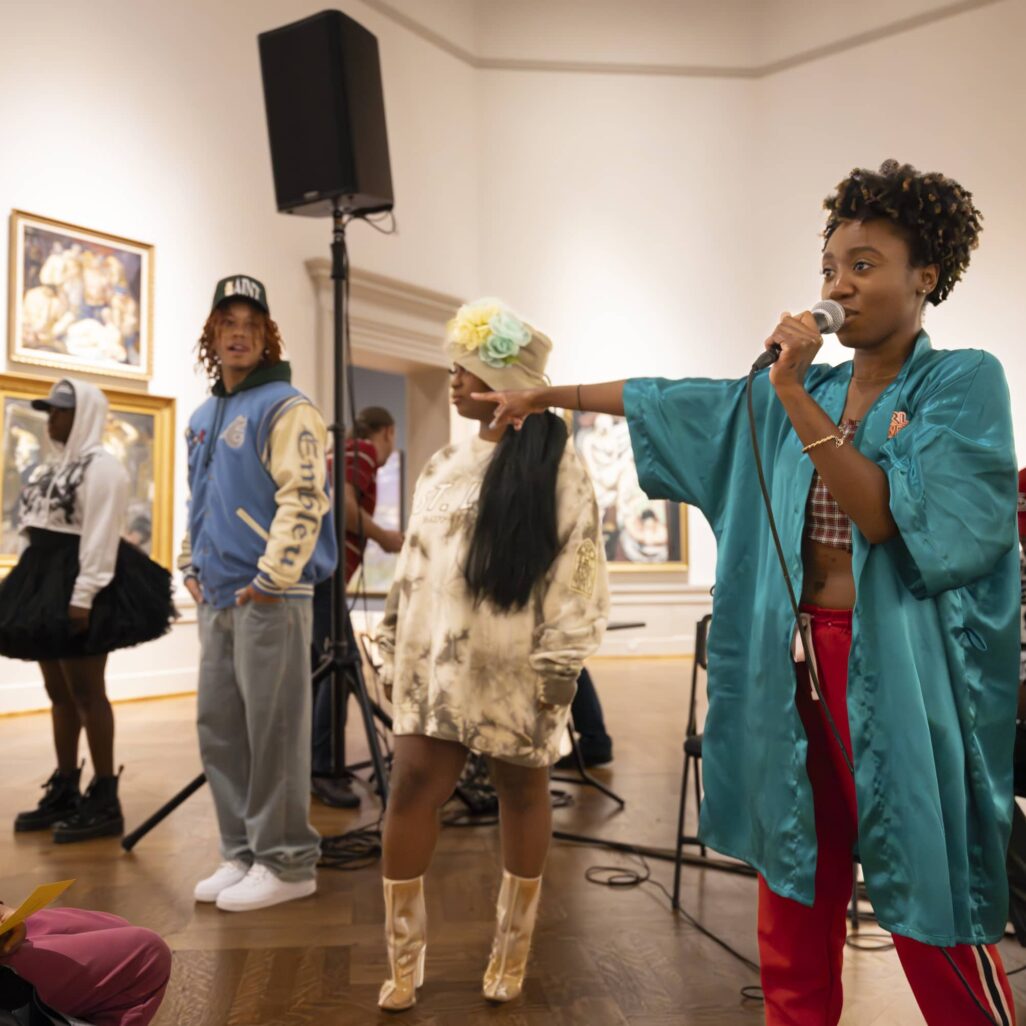 Woman with microphone speaking to group in art gallery.