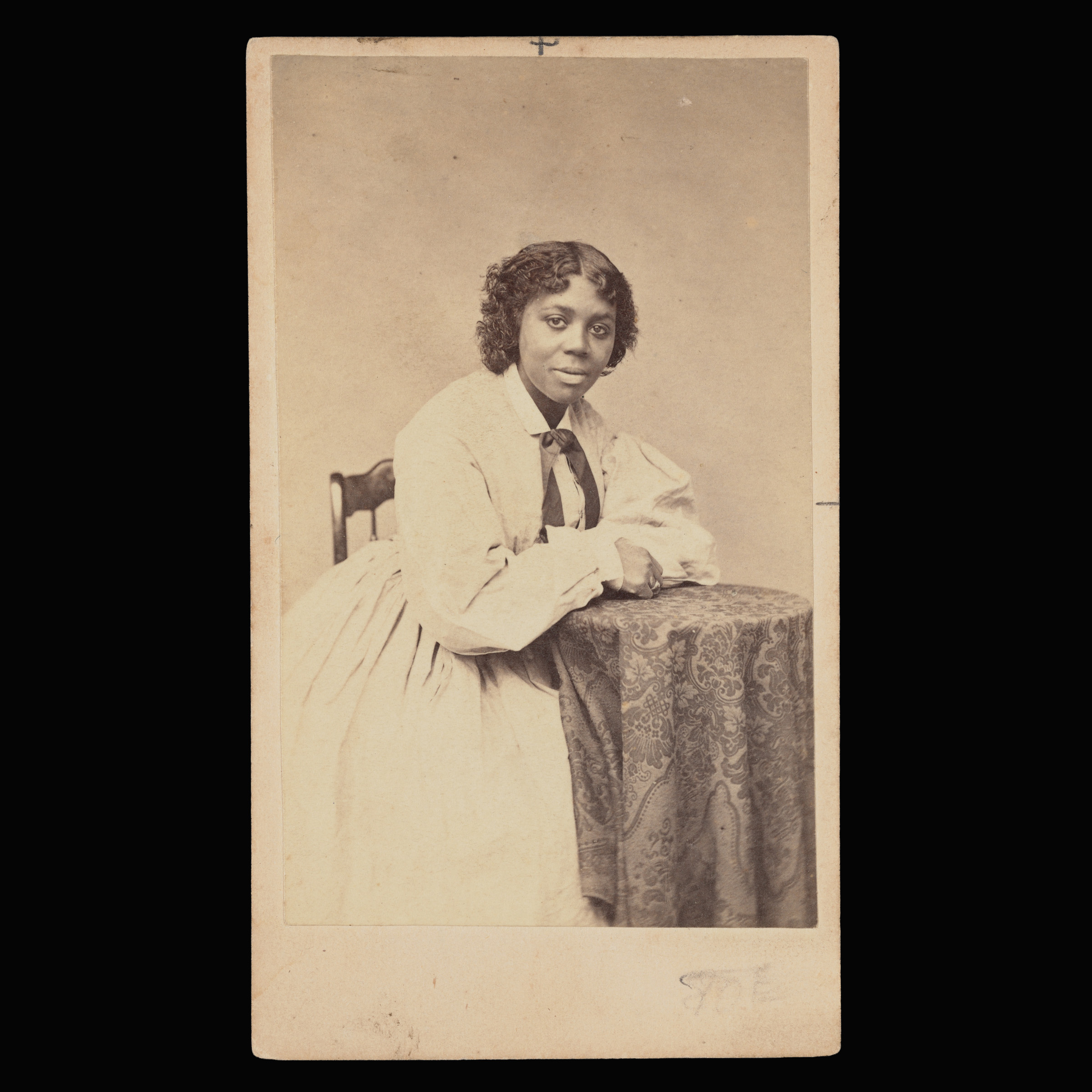 An archival photograph depicting a Black woman facing the camera and seated at a small table.