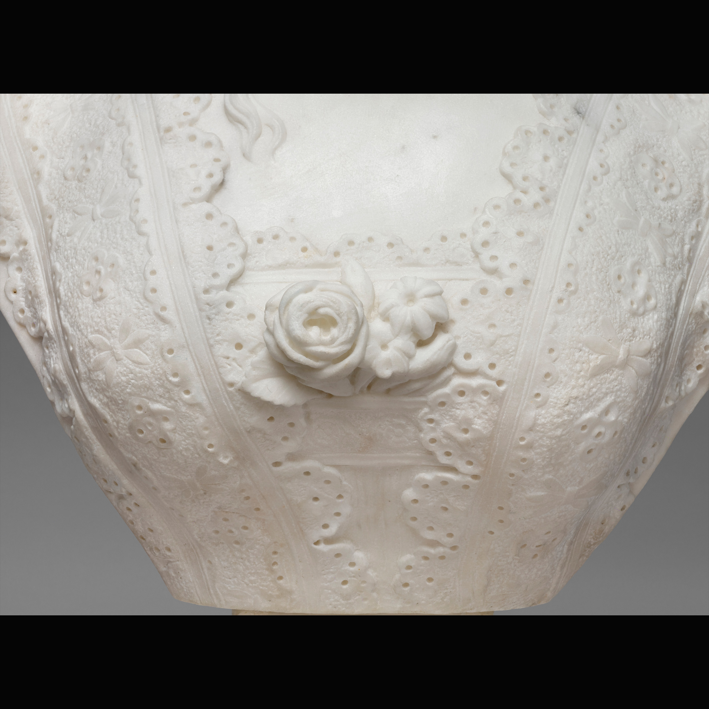 Zoomed in perspective of lace and flowers on the dress of a marble statue.