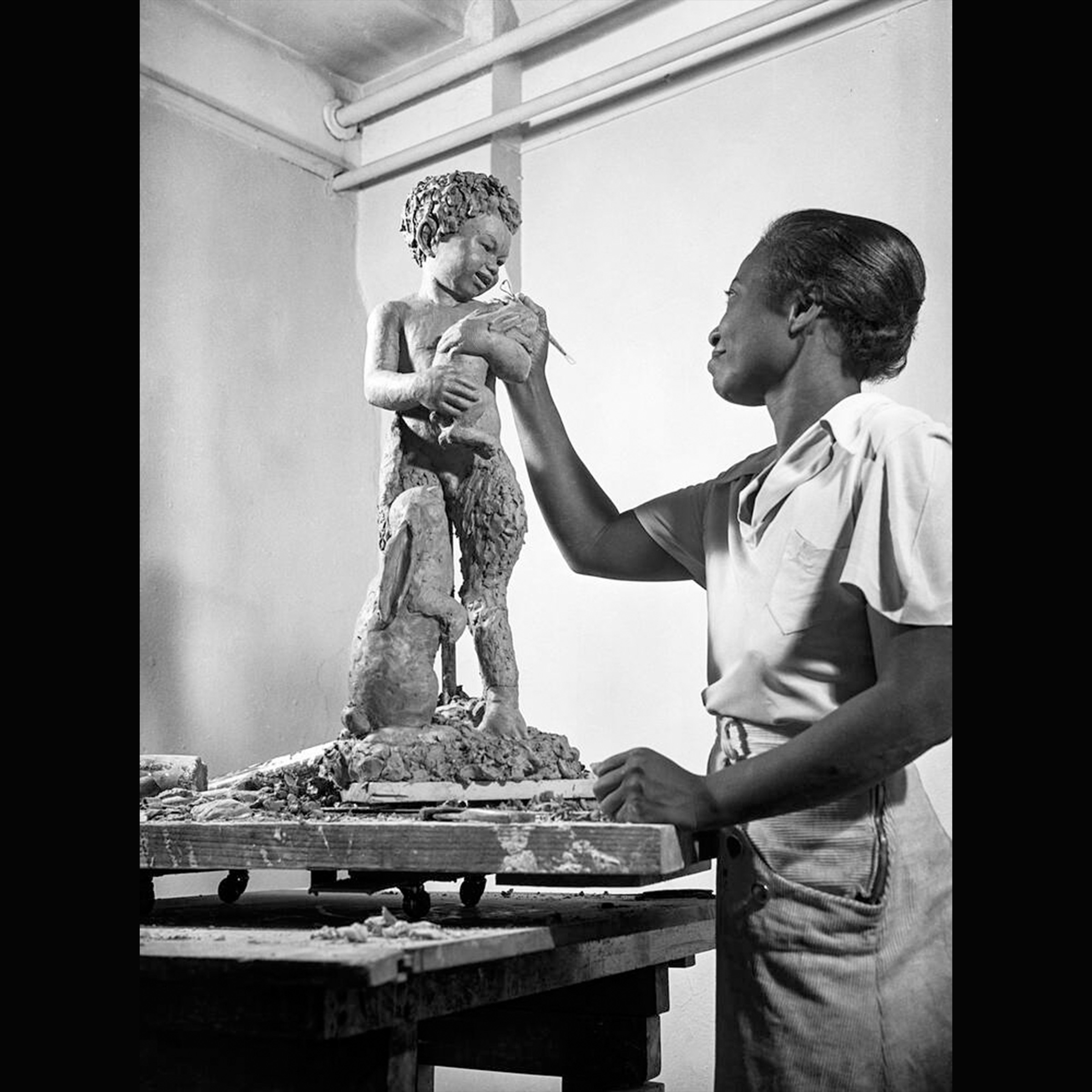 Black woman artist places right hand on a sculpture in progress at an art studio.