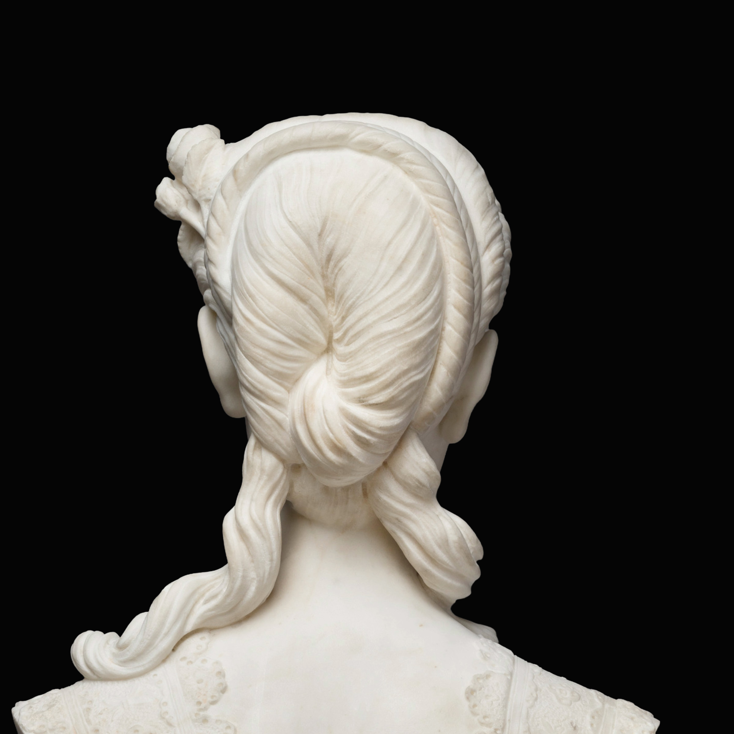 Back view of a marble statue depicting a woman from the shoulders up, with a 19th century hairstyle.